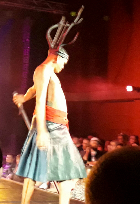 Antlers and Crown headdress made of wire covered in black leather Macbeth wears a kilt made of black leather slashed showing dark/bright Blue cloth.Red velvet cummerbund with huge black leather buckle & ties hanging down their hips. Macbeth holds a tall black sword.