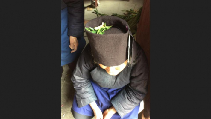 Dong Woman in temple with fresh herbs in crown of her hat