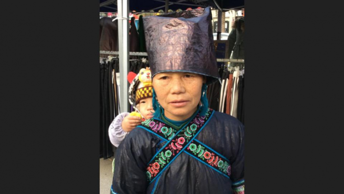 Dong woman wearing jacket & hat of beaten, ‘Shiny’ indigo. Embroidered straps of Baby Carrier.